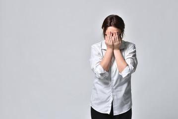 A tired woman in a black protective mask covers her face with her hands against a white background, during the coronavirus pandemic. The concept of viral danger, stress and fear.