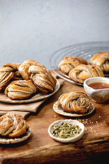 Traditional Swedish cardamom sweet buns Kanelbulle on plate, ingredients in ceramic bowl above on wooden table.