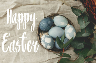 Happy Easter text. Easter greetings lettering. Modern blue Easter eggs on vintage plate on rustic table with spring flowers and eucalyptus. Greeting card © sonyachny