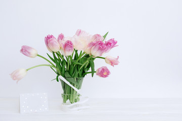 Tulip flowers in glass vase with gift card over white background isolated