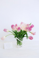 Obraz na płótnie Canvas Tulip flowers in glass vase with gift card over white background isolated