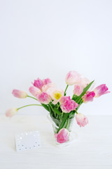 Tulip flowers in glass vase with gift card over white background isolated