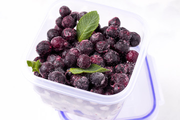 frozen blackcurrant berries on a white plate in a glass container