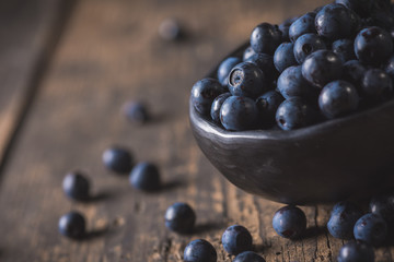 Clay bowl with organic, wild forest blueberries on a rustic wooden table.