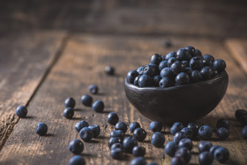 Clay bowl with organic, wild forest blueberries on a rustic wooden table.
