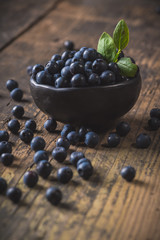 Clay bowl with organic, wild forest blueberries on a rustic wooden table.