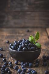 Clay bowl with organic, wild forest blueberries on a rustic wooden table.