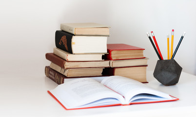 Home office: open textbook, notebook, stack of old books retro education back to school background, glasses and pencils in holder with copy space for text.