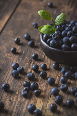 Clay bowl with organic, wild forest blueberries on a rustic wooden table.