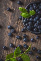 Clay bowl with organic, wild forest blueberries on a rustic wooden table.