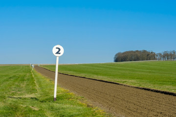 2 furlong distance marker seen on the edge of a professional flat-racing training track in the UK. The track extends up an incline and then bends right near a wooded area.