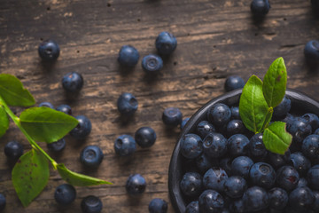 Clay bowl with organic, wild forest blueberries on a rustic wooden table.