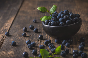 Clay bowl with organic, wild forest blueberries on a rustic wooden table.