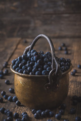 Copper bucket with organic, wild forest blueberries on a rustic wooden table.