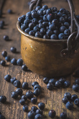 Copper bucket with organic, wild forest blueberries on a rustic wooden table.