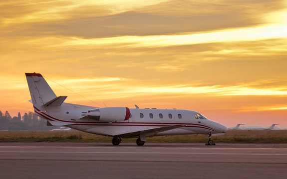 Private airplane parked at the airport at sunset.  Jet plane parking at the airport on the beautiful sunset background. Small private airplane at the airport parking with fantastic sunrise.