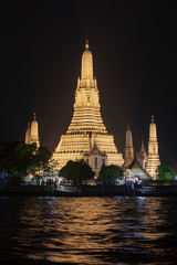 Naklejka premium Arun Temple, one of the most famous in Bangkok, Taliandia, stands up, illuminated at night, on the banks of the Chao Phraya River with its troubled waters.