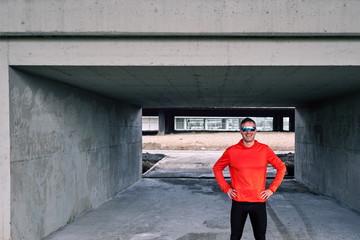 Attractive sportsman standing under the bridge posing and looking at camera. Exercise alone.