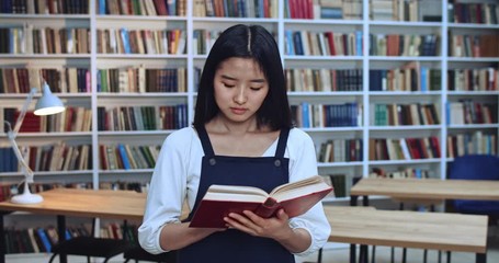 Portrait of smart asian librarian with black hair learning from the book in library.