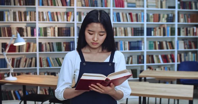Portrait of smart asian librarian with black hair learning from the book in library.