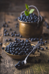 Brass plate with organic, wild forest blueberries on a rustic wooden table.