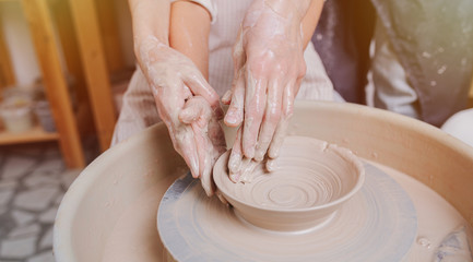 Children's and adults's hands together working behind the potter's wheel