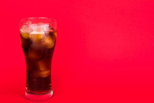 Cola with ice in a large glass on a red background. Copy space.