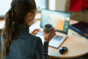 Blured image woman freelancer sitting at desk, enjoying coffee, using laptop computer. Skilled...