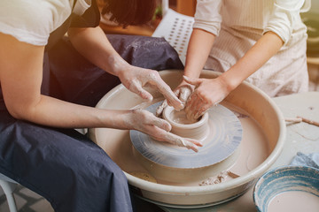 Children's and adults's hands together working behind the potter's wheel.