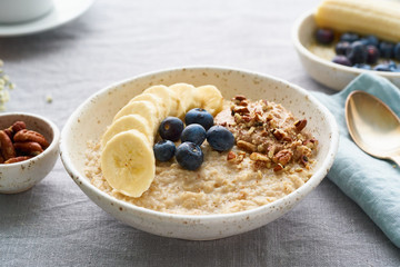 Whole oatmeal, large bowl of porridge with banana, blueberries, nuts for breakfast,