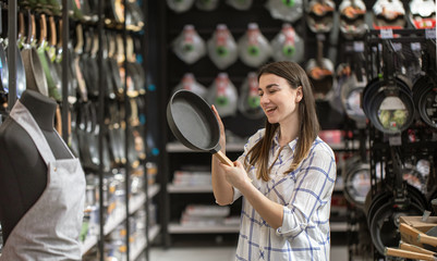 A young woman in the store chooses a frying pan .