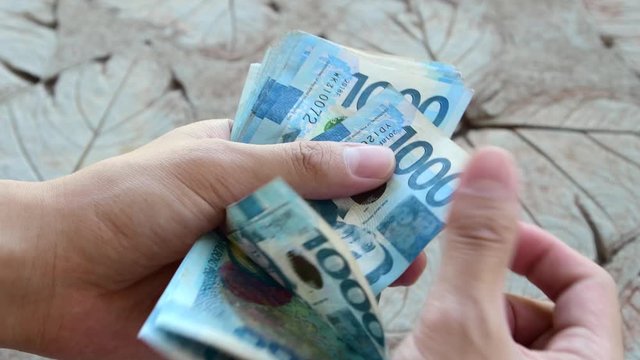 Counting a bulk of 1000 Philippine peso cash on a table by hand