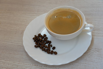 Top view of a cup of coffee and coffee beans on white plate