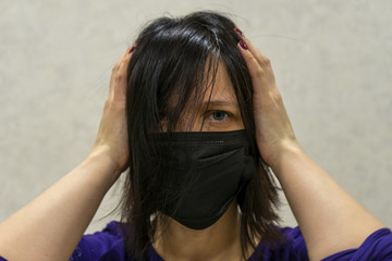 A woman in a black medical mask holds her head in despair