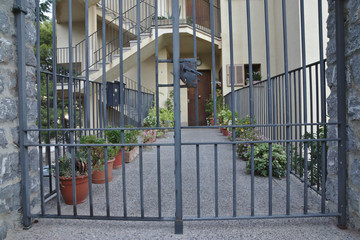 Closed gate in front of a walkway with potted flowers to a house