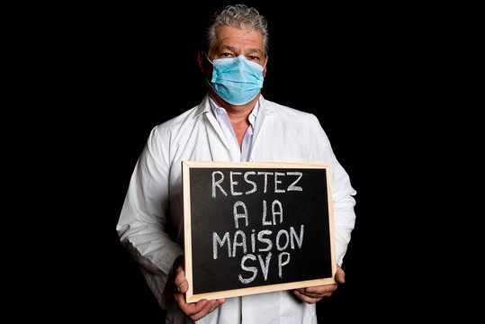 Physician with mask holding a chalkboard on which is written stay home in french