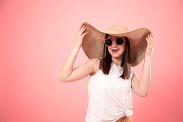 Portrait of a young woman in a summer hat and glasses, on a pink background .