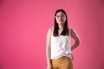 Portrait of a young woman with glasses on a pink background.