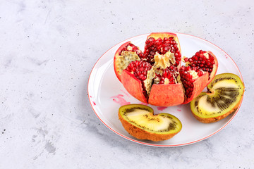 Ripe pomegranate and kiwi on a white porcelain plate on a background of gray concrete.
