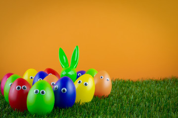 Gruppe von Ostereiern mit Augen und einem Osterhasen vor orangem Hintergrund