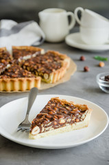 Tart with chocolate caramel, hazelnuts, peanuts, almonds and seed mix on a dark concrete background. Vertical orientation.