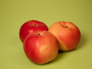 three red and yellow apples isolated on a green background