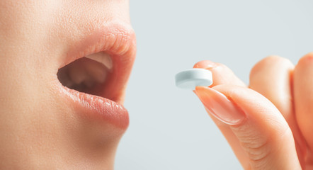Woman taking a white round pill, view of mouth.