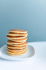 Stack of american pancakes on a white table on blue background. Copyspace. Breakfast and snack