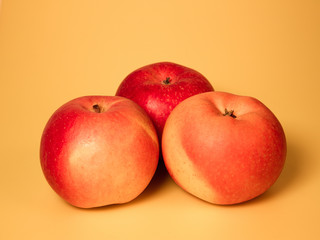 three red and yellow apples isolated on a beige background