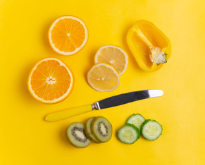 Orange, lemon, kiwi, cucumber and yellow knife on a yellow background.