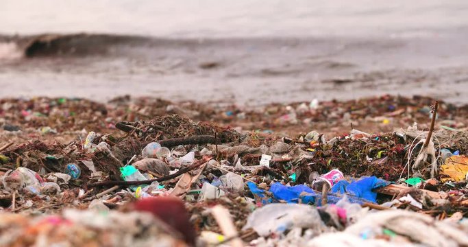 Plastic trash and garbage dumped on dark sand of the beach and floating on the surface of the ocean water. Environmental and water pollution problem concept. Marine pollution killing wildlife.