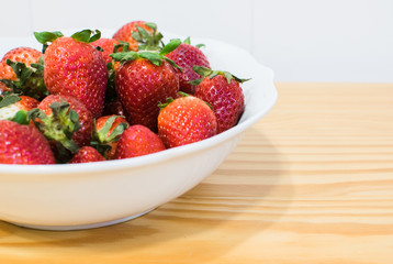 Close-up de fresas en un bol blanco sobre mesa de madera