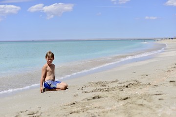Fototapeta na wymiar A boy sits on a beautiful beach. Copy space for text.