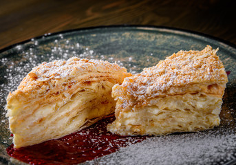 Layered cake with cream Napoleon in plate on wooden table background